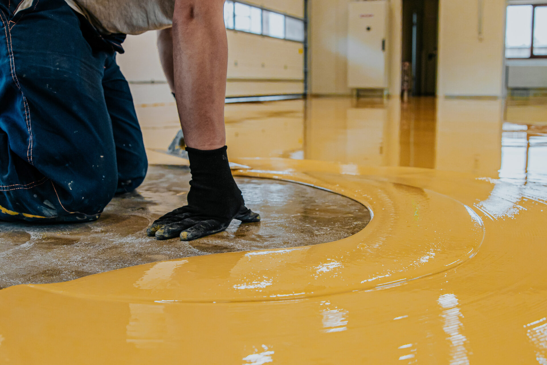 Worker, coating floor with self-leveling epoxy resin in industri